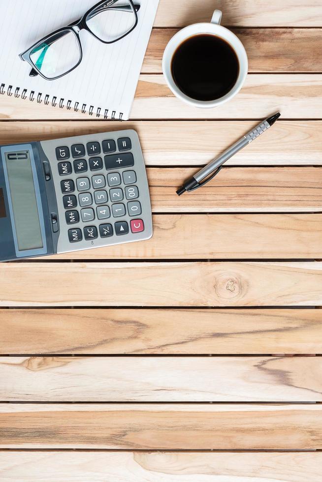 Draufsichtschreibtisch mit Taschenrechner, Stift, Brille, leerem Notizbuch und Kaffeetasse auf Holztischhintergrund. arbeitsbereich oder home office mit kopierraum für textkonzept foto