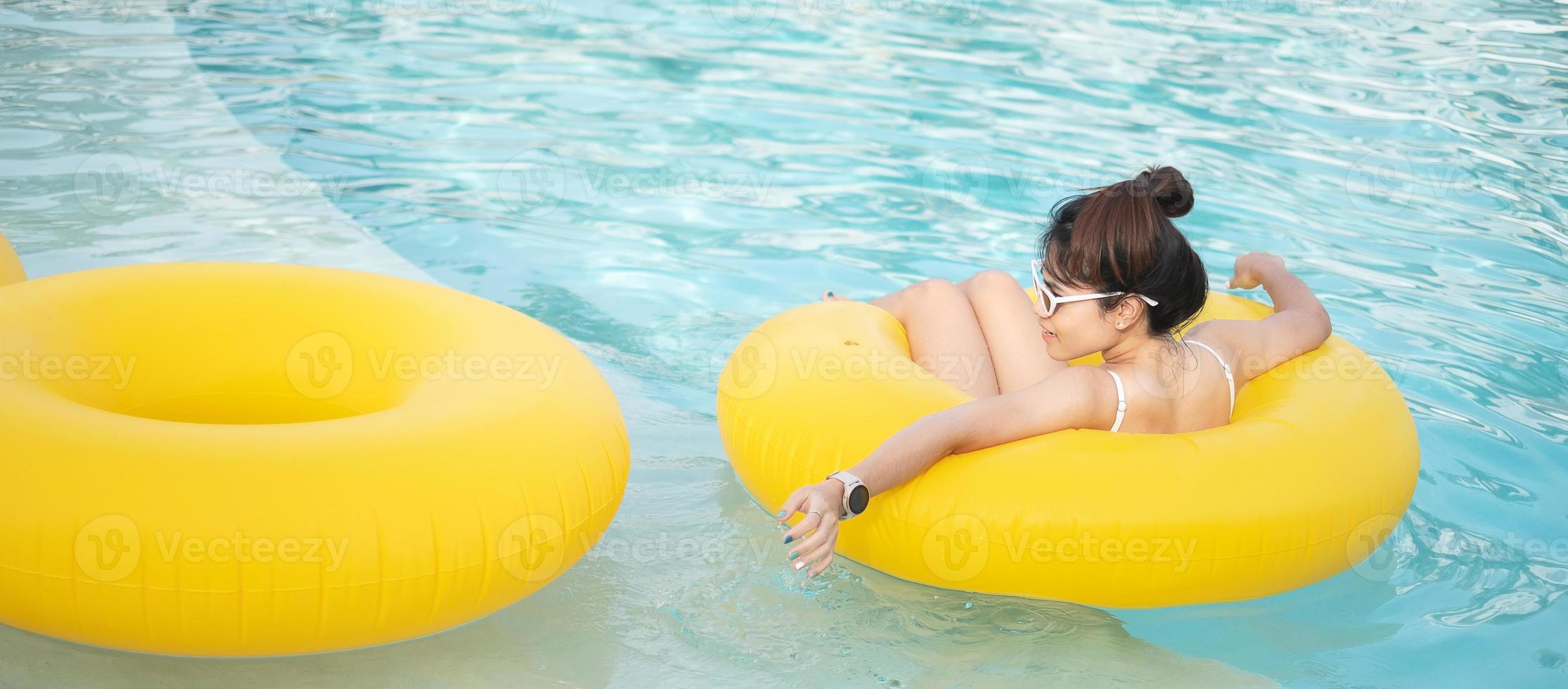 glückliche frau im weißen badeanzug mit gelbem schwimmring im luxus-poolhotel, junge frau mit sonnenbrille genießt im tropischen resort. entspannendes, sommerreise-, urlaubs-, urlaubs- und wochenendkonzept foto