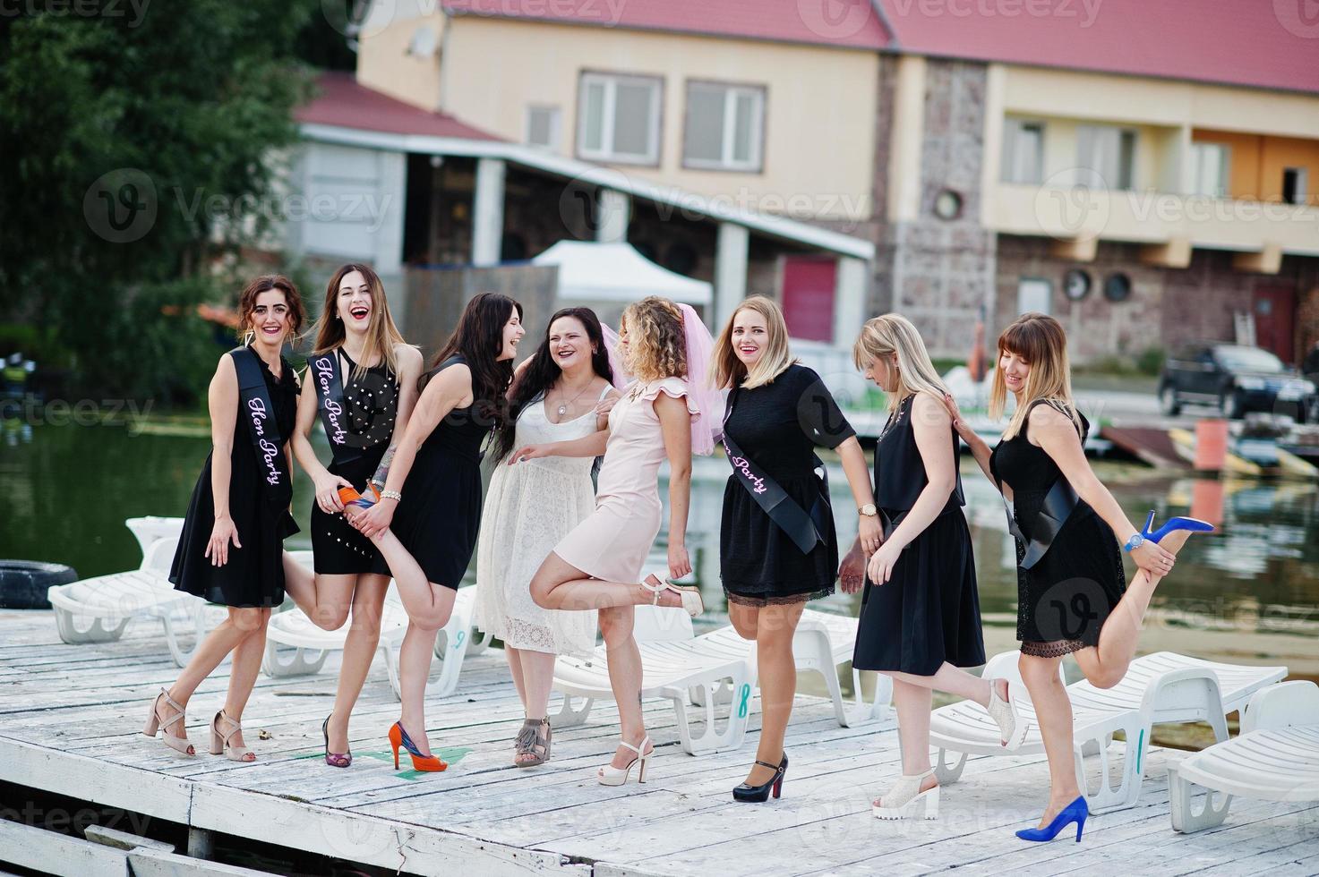 Gruppe von 8 Mädchen in Schwarz und 2 Bräute beim Junggesellinnenabschied am Pier am Strand. foto