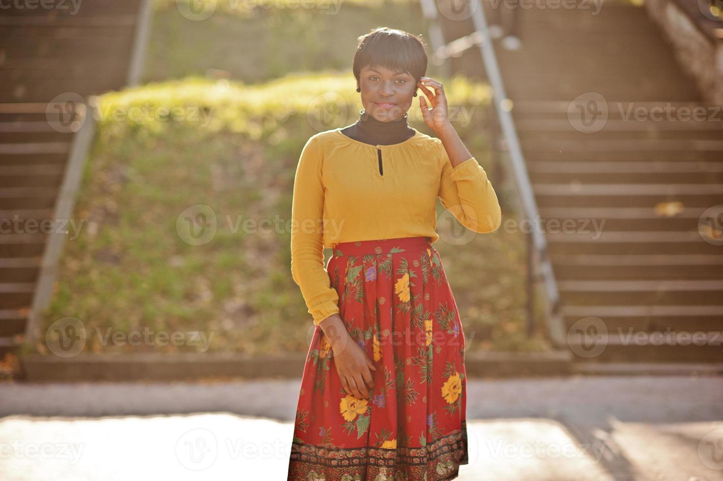 afroamerikanisches Mädchen im gelben und roten Kleid im goldenen Herbstpark. foto