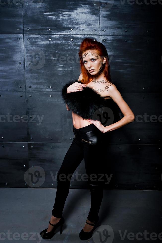 Model rothaariges Mädchen mit ursprünglich Make-up wie Leoparden-Raubtier gegen Stahlwand. Studioportrait. foto