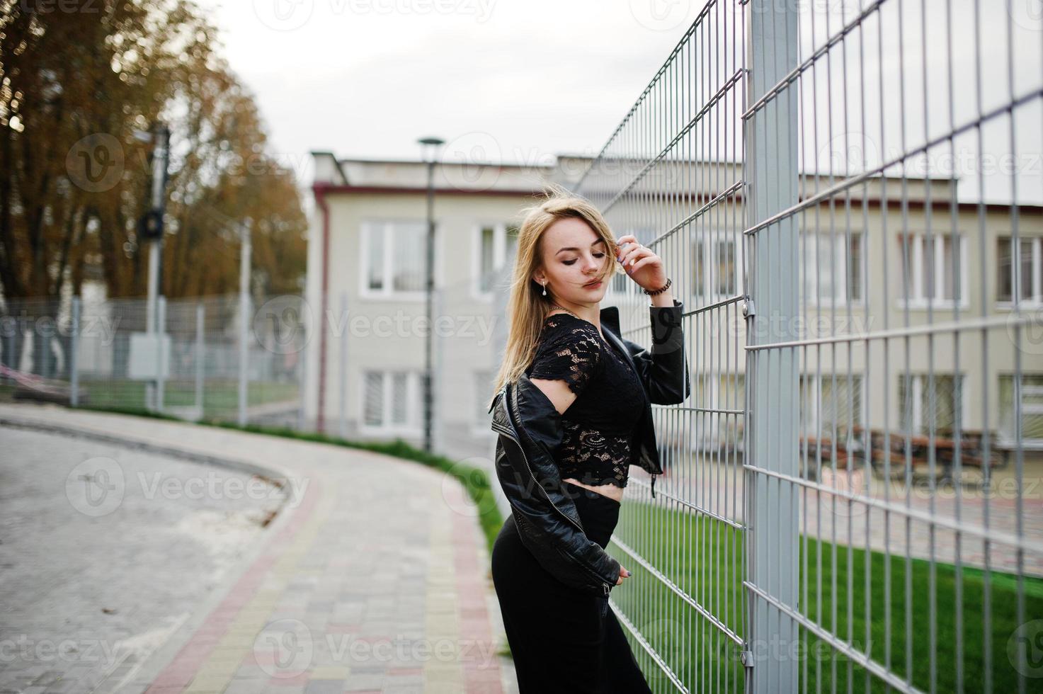 elegante blonde mädchen tragen auf schwarz, die auf den straßen der stadt gegen eisenkäfig posieren. foto