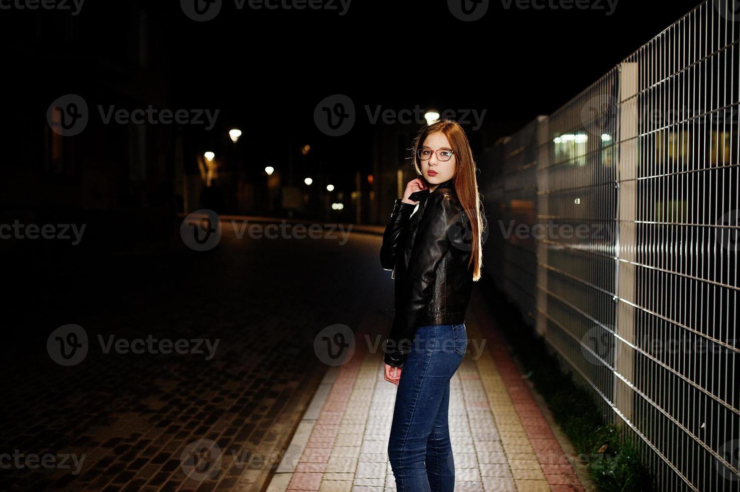 Nachtporträt von Mädchen Model Wear auf Jeans und Lederjacke gegen Eisenzaun. foto