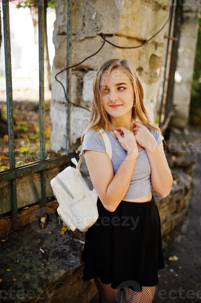 Junges blondes Mädchen im schwarzen Rock mit Frauenrucksack auf der Straße gestellt. foto