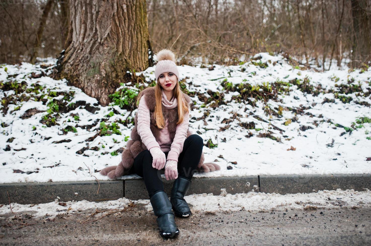 Stilvolles Mädchen in Pelzmantel und Kopfbedeckung am Wintertag am Straßenrand. foto