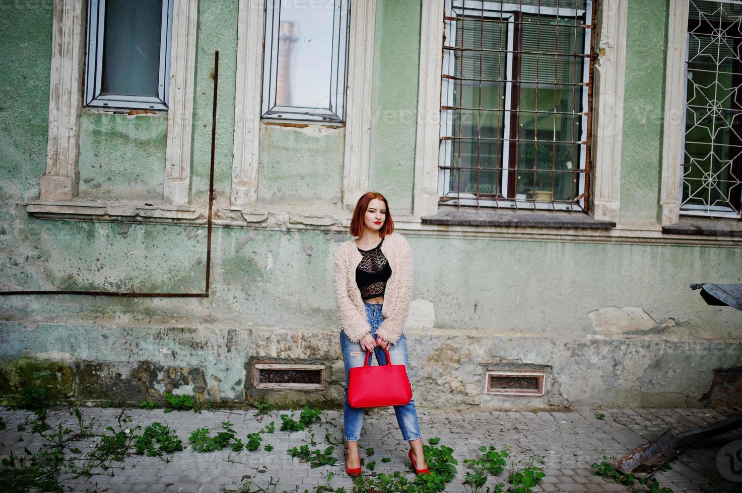 Rothaariges Mädchen mit roter Handtasche posierte auf der Straße der Stadt. foto