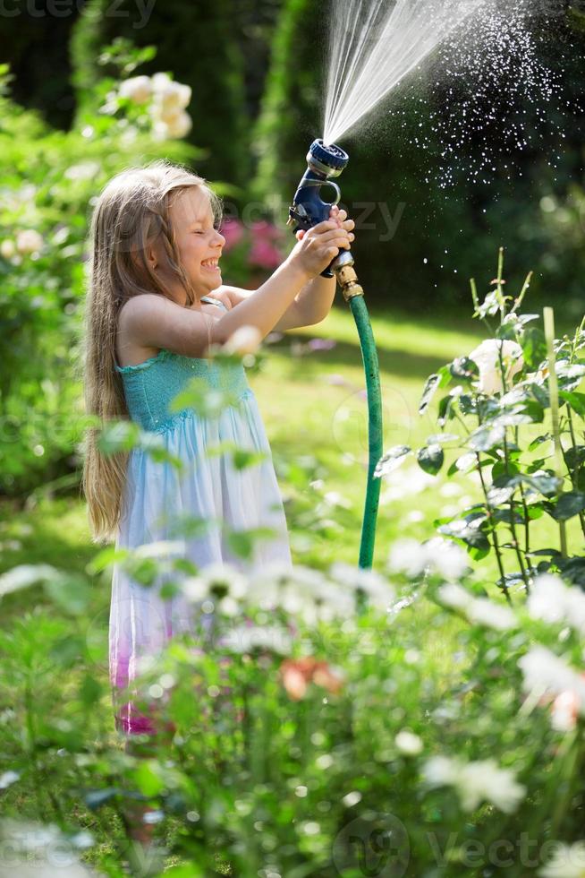 Mädchen, das Pflanzen mit Gartenschlauch gießt foto