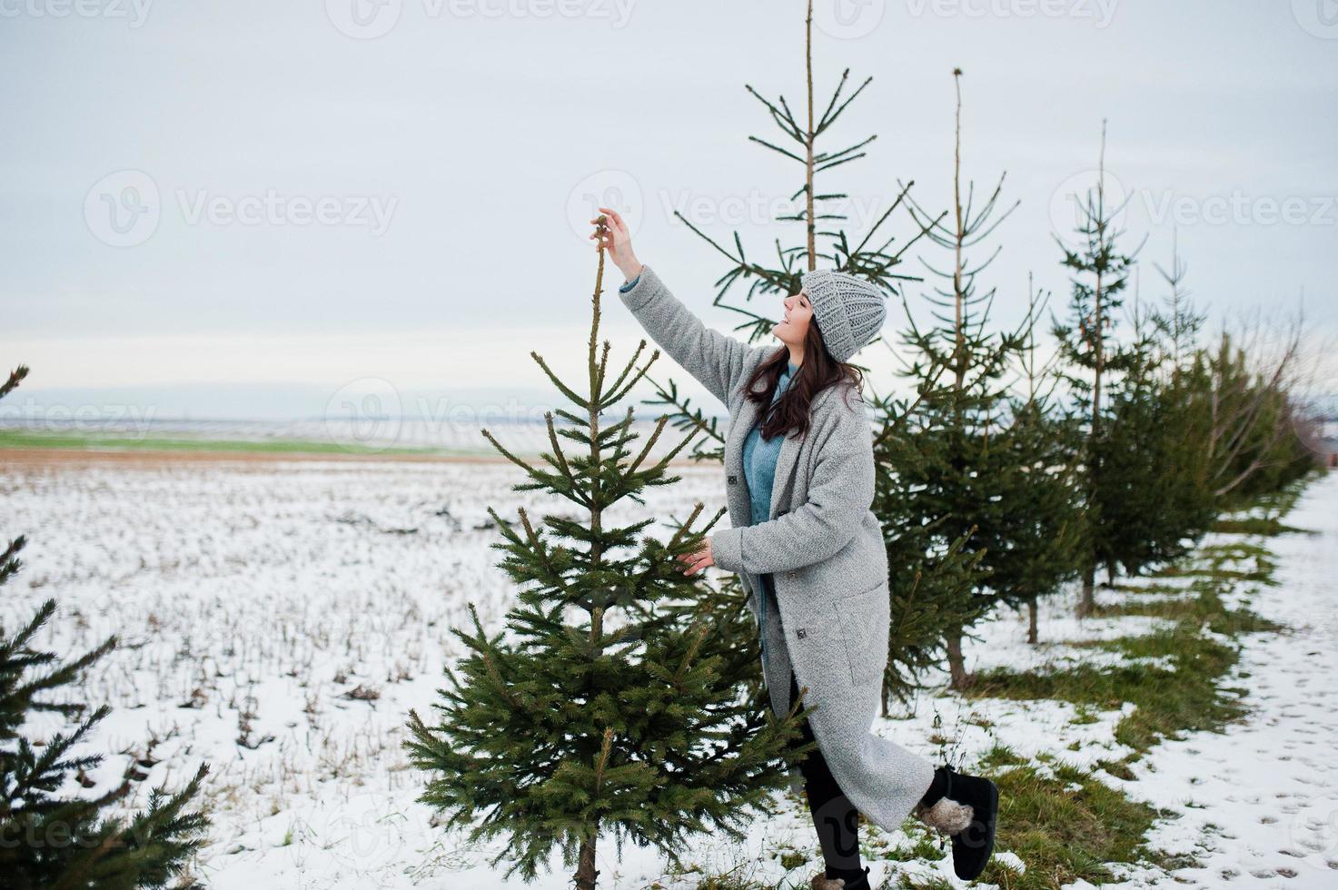 Porträt eines sanften Mädchens in grauem Mantel und Hut gegen den Neujahrsbaum im Freien. foto