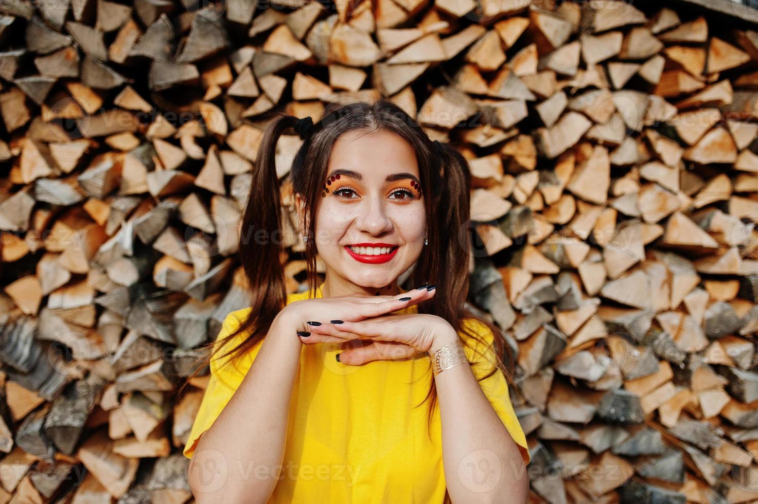 junges lustiges mädchen mit hellem make-up, schwanzhaarabnutzung auf gelbem hemd gegen hölzernen hintergrund. foto