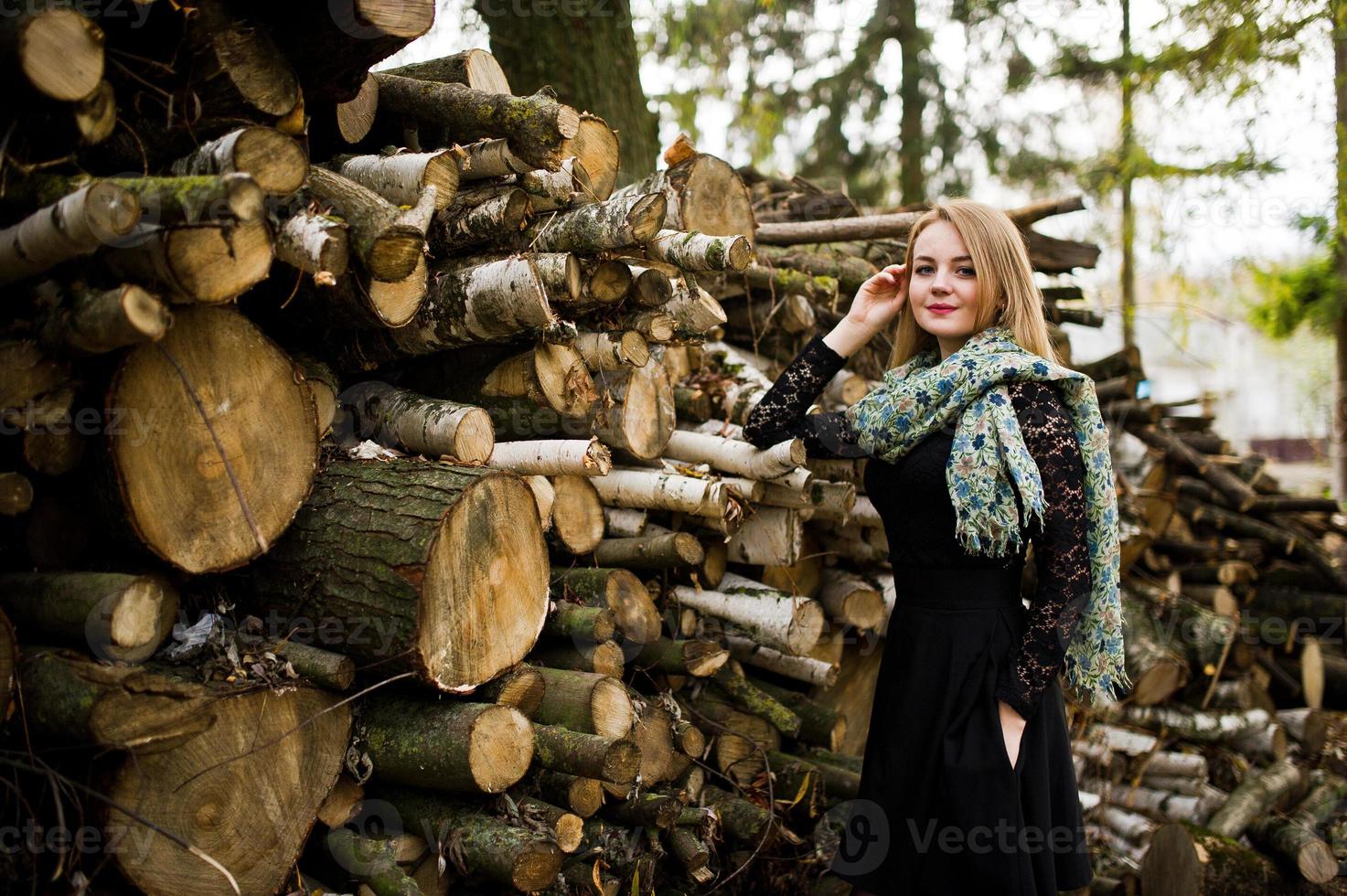 junges blondes Mädchen in Schwarz mit Schal posierte vor Holzstümpfen Hintergrund. foto