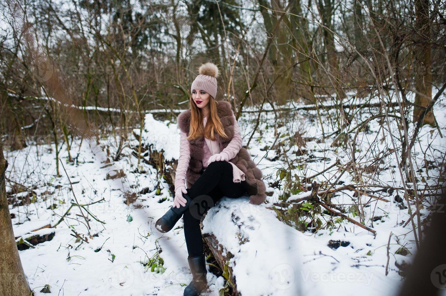 stilvolles Mädchen in Pelzmantel und Kopfbedeckung im Winterwald. foto