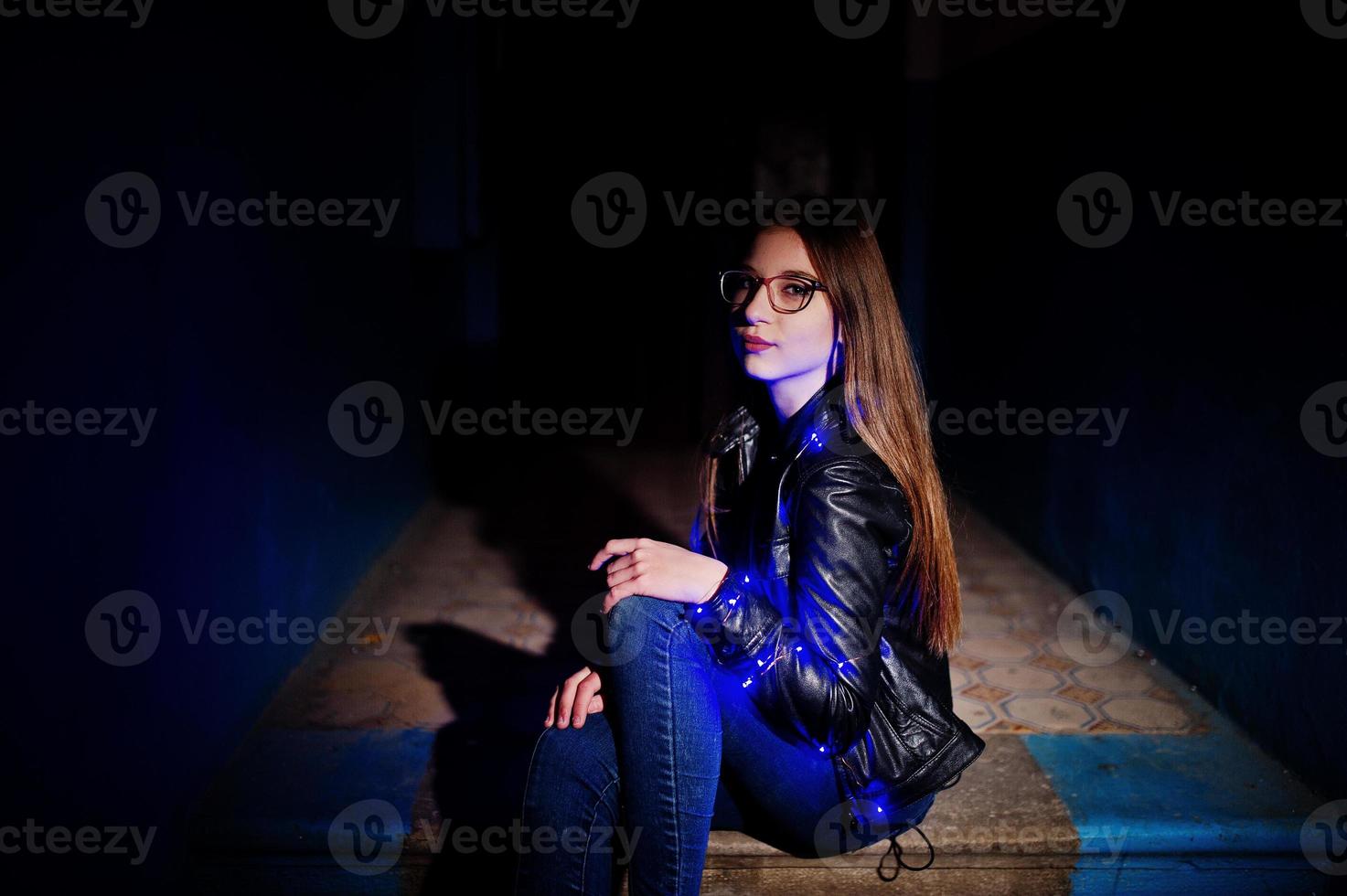 Nachtporträt von Mädchen Model Wear auf Brille, Jeans und Lederjacke, mit blauer Girlande auf ihr. foto