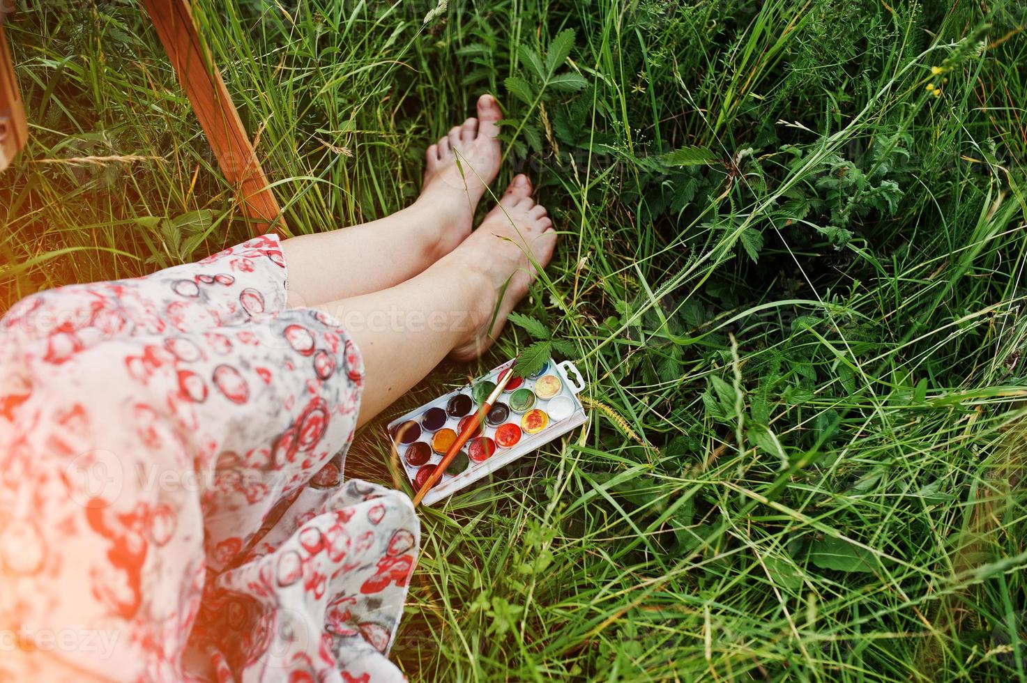 Nahaufnahmefoto von weiblichen Beinen auf dem hohen Gras zusammen mit Aquarellpalette. foto