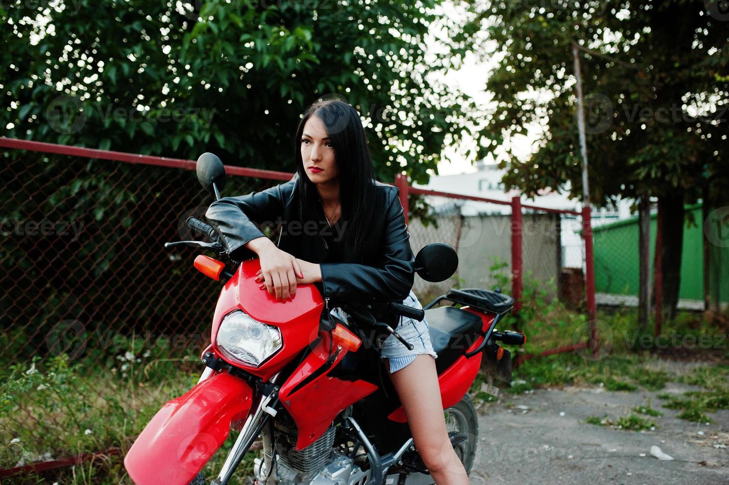 Porträt einer coolen und fantastischen Frau in Kleid und schwarzer Lederjacke, die auf einem coolen roten Motorrad sitzt. foto