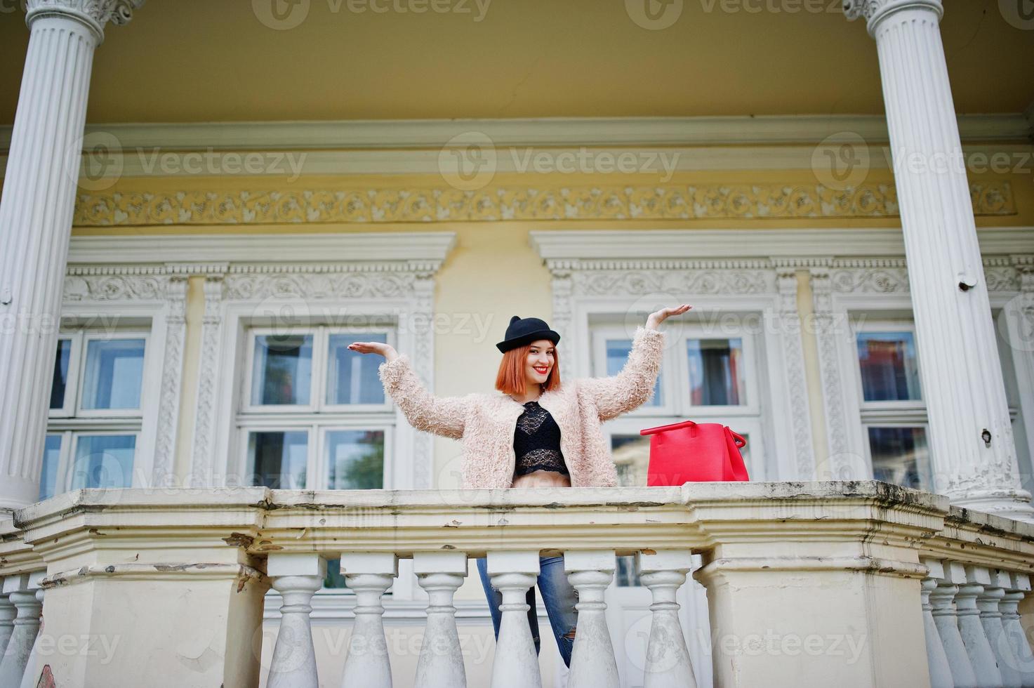 Rothaariges Mädchen mit Brille und Hut mit roter Handtasche posierte in der Nähe eines Vintage-Hauses. foto