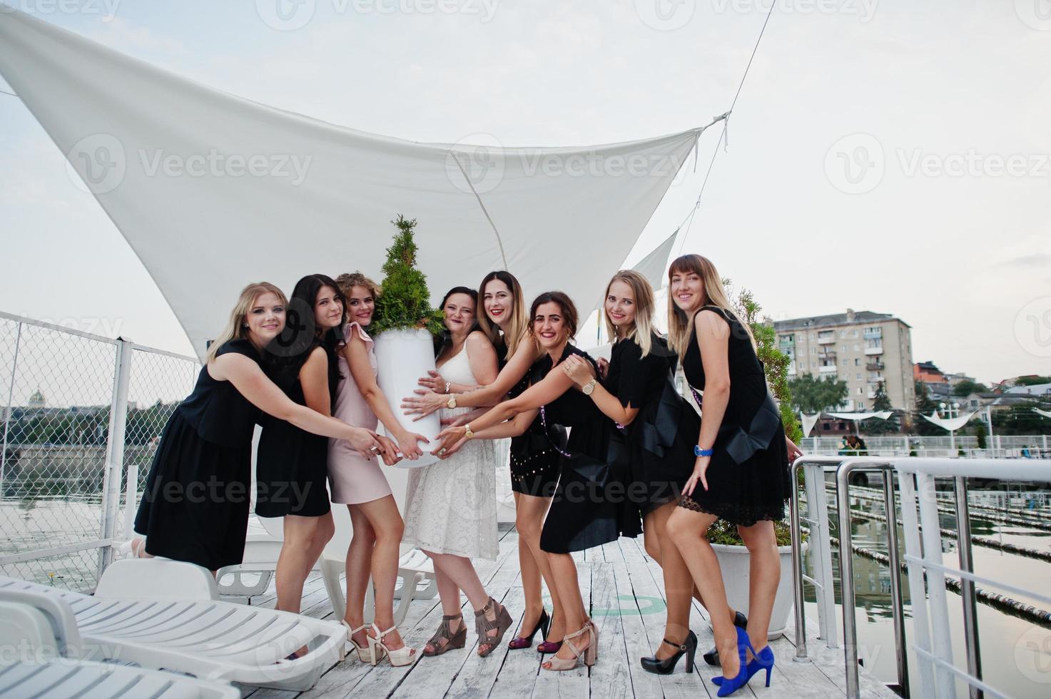 Gruppe von 8 Mädchen in Schwarz und 2 Bräute beim Junggesellinnenabschied, die sich am Pier am Strand vergnügen. foto