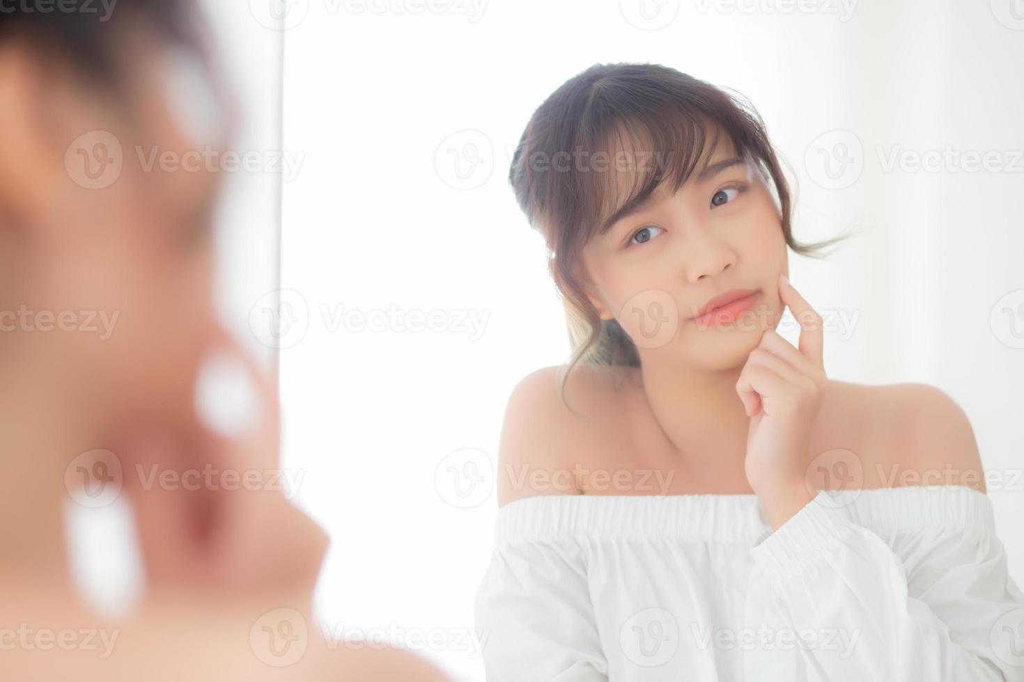 schönes gesicht junge asiatische frau mit glücklich lächelndem und aussehendem spiegel, make-up von schönheitsgesichtsmädchen mit hautpflege und kosmetischer behandlung, erfrischung von frau und sauber für charmantes, gesundes konzept. foto