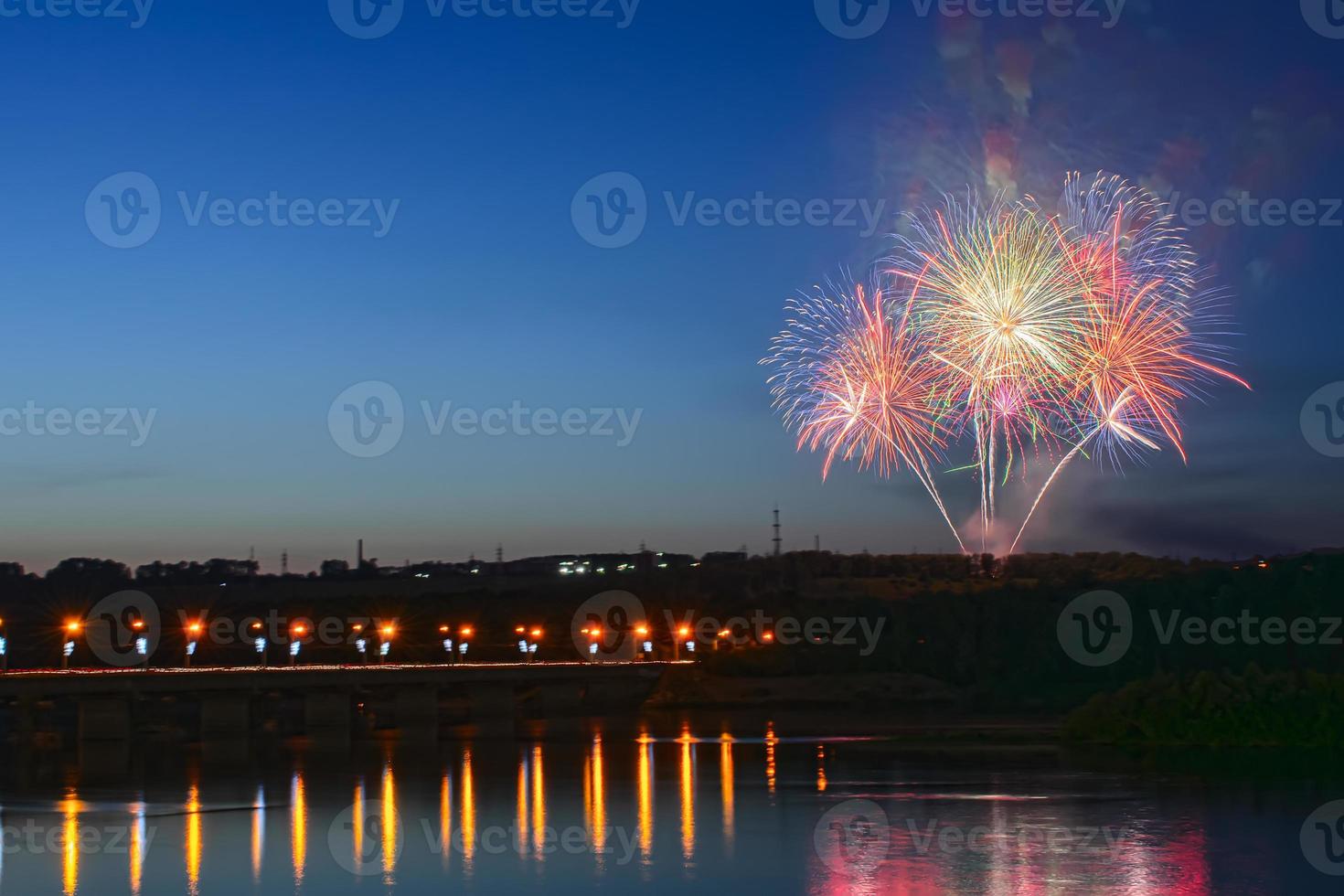 Feuerwerk auf dem Hintergrund eines klaren Nachthimmels in der Nähe des Flusses und der Brücke foto