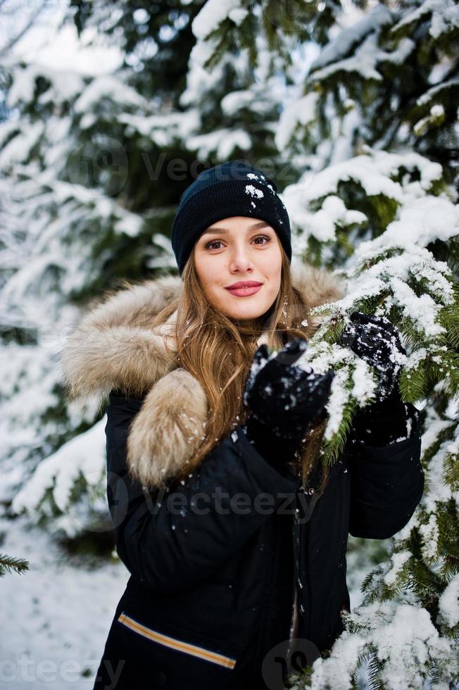 schönes brünettes Mädchen in warmer Winterkleidung. Modell auf Winterjacke und Hut in der Nähe von Pinien. foto