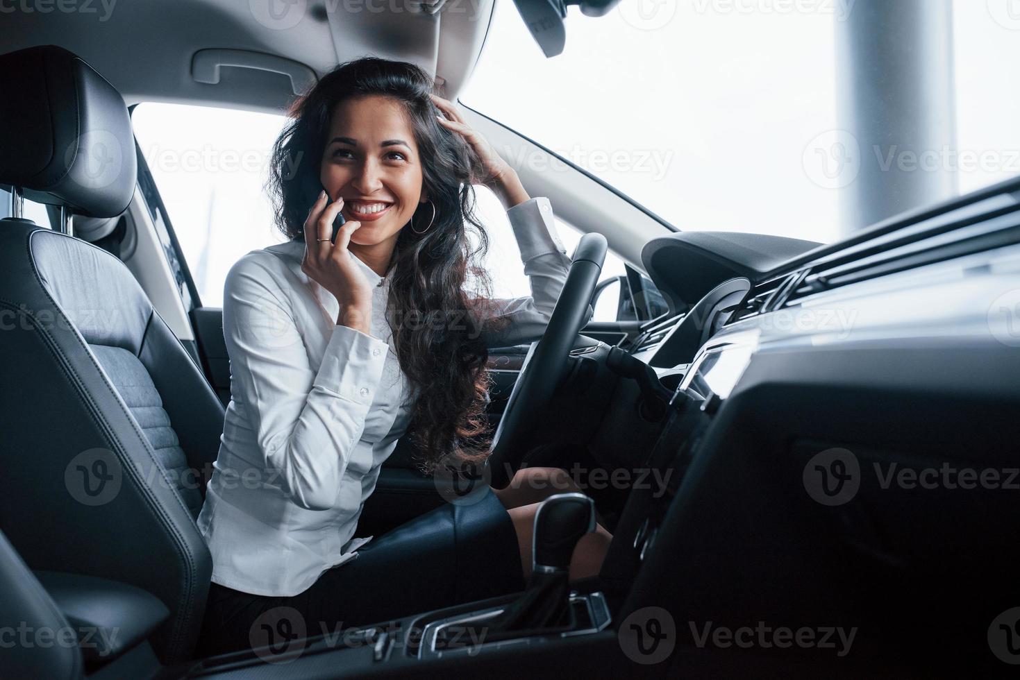Freund ruft an. schöne geschäftsfrau, die ihr neues auto im autosalon probiert foto