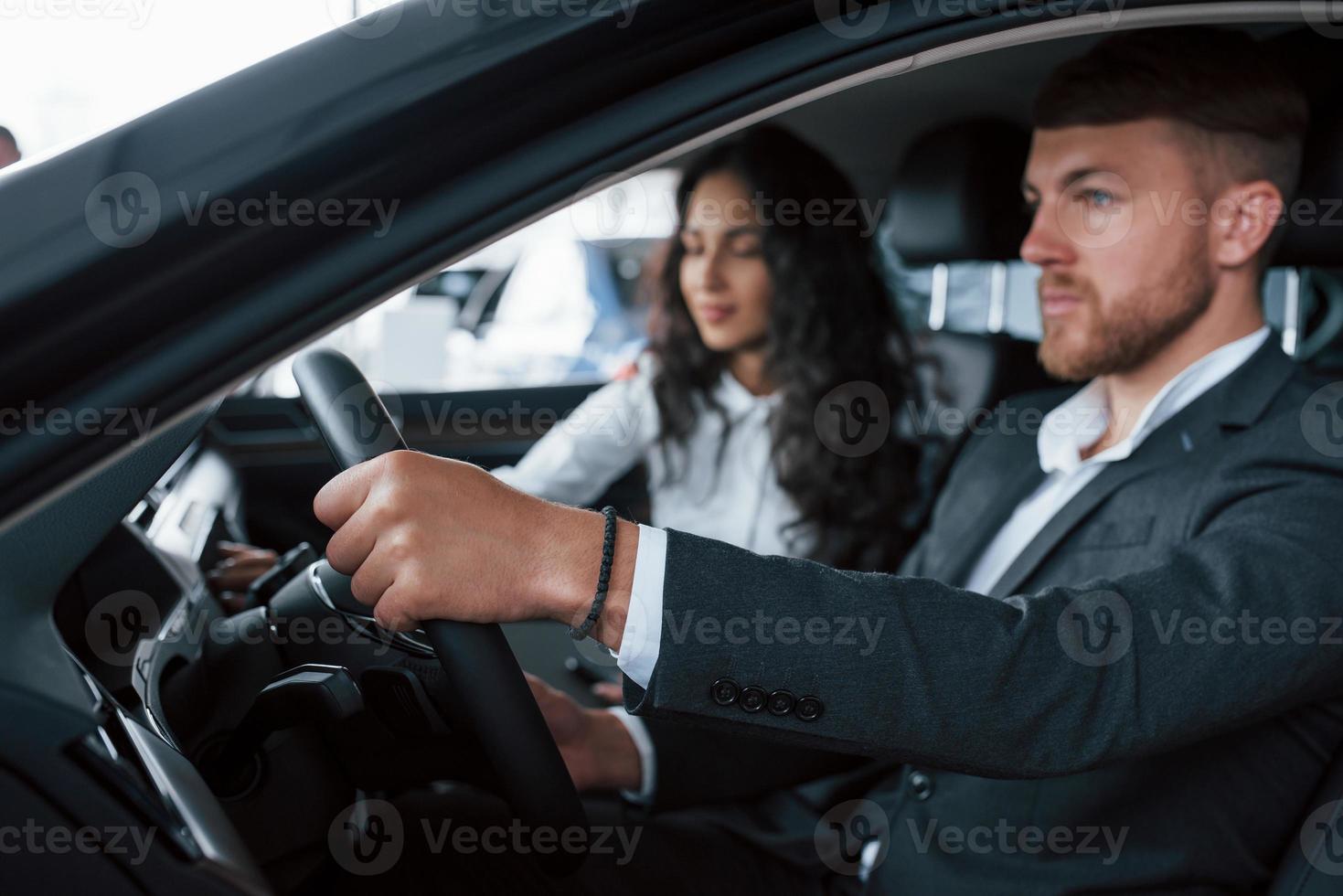 konzentriert aufs Fahren. Schönes erfolgreiches Paar, das im Automobilsalon ein neues Auto ausprobiert foto
