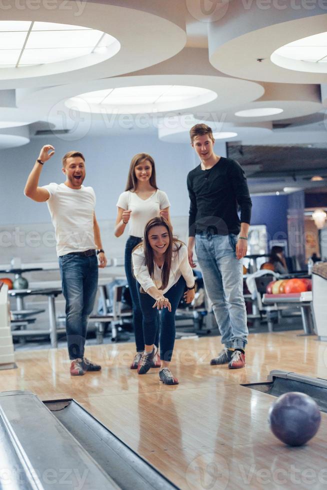 Komm schon, streik. Junge, fröhliche Freunde haben an ihren Wochenenden Spaß im Bowlingclub foto