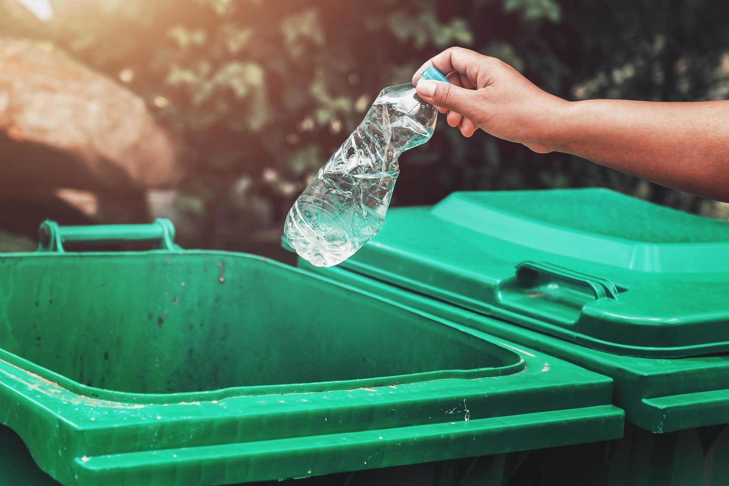 Frauenhand, die Müllplastikflasche aufhebt, die zur Reinigung im Park in den Müll geworfen wird foto