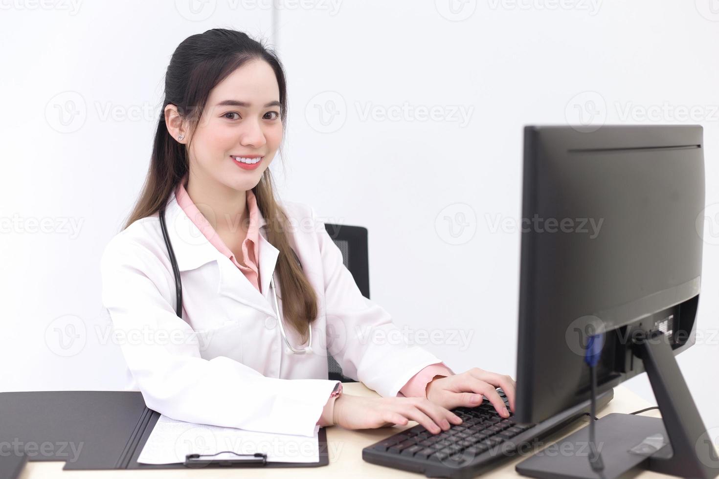 Die asiatische Ärztin tippt auf der Tastatur, um Informationen in den Computer aufzunehmen, während sie im Krankenhaus eine medizinische Gesichtsmaske trägt. foto