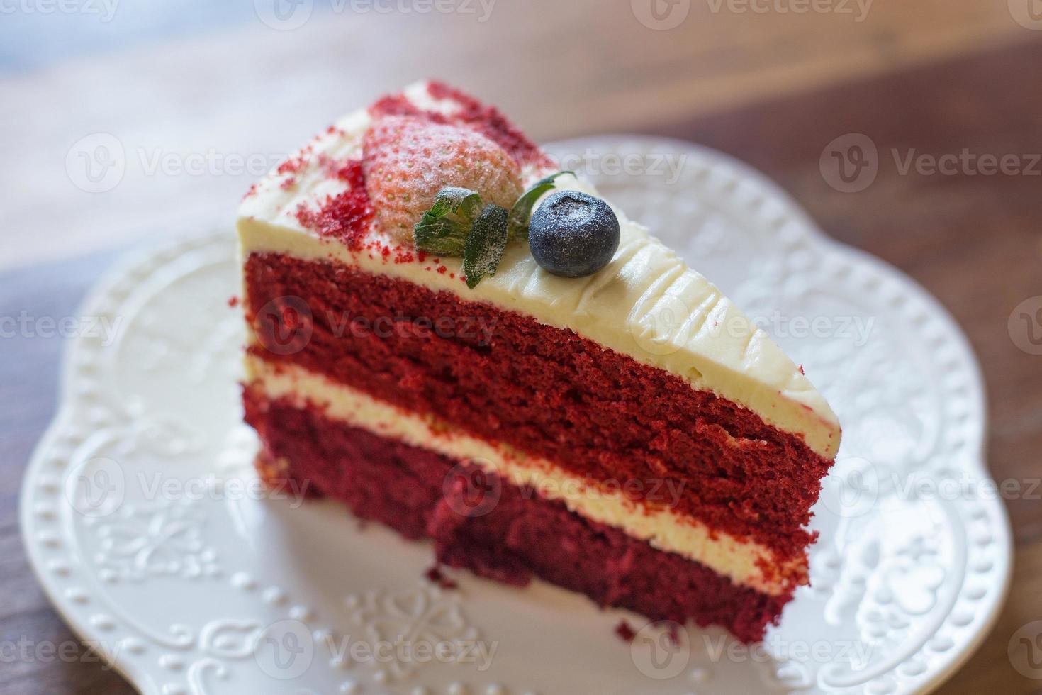 Roter Samtkuchen mit Buttercreme-Zuckerguss, dekoriert mit Erdbeeren und Heidelbeeren auf einem weißen Teller. foto