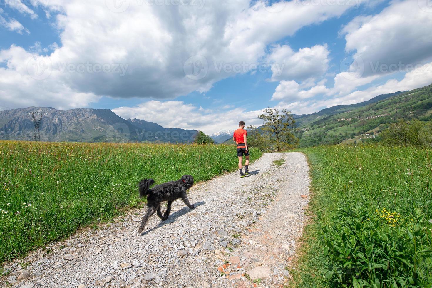 Mann beim Spaziergang in den Bergen mit seinem Hund, der ihm folgt foto