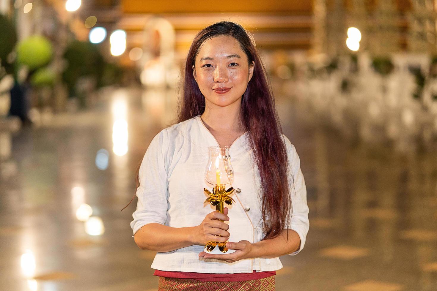 porträt junge asiatische frau lächelt und trägt traditionelles kleid von thailand, das kerze am wat suthat thepwararam hält foto