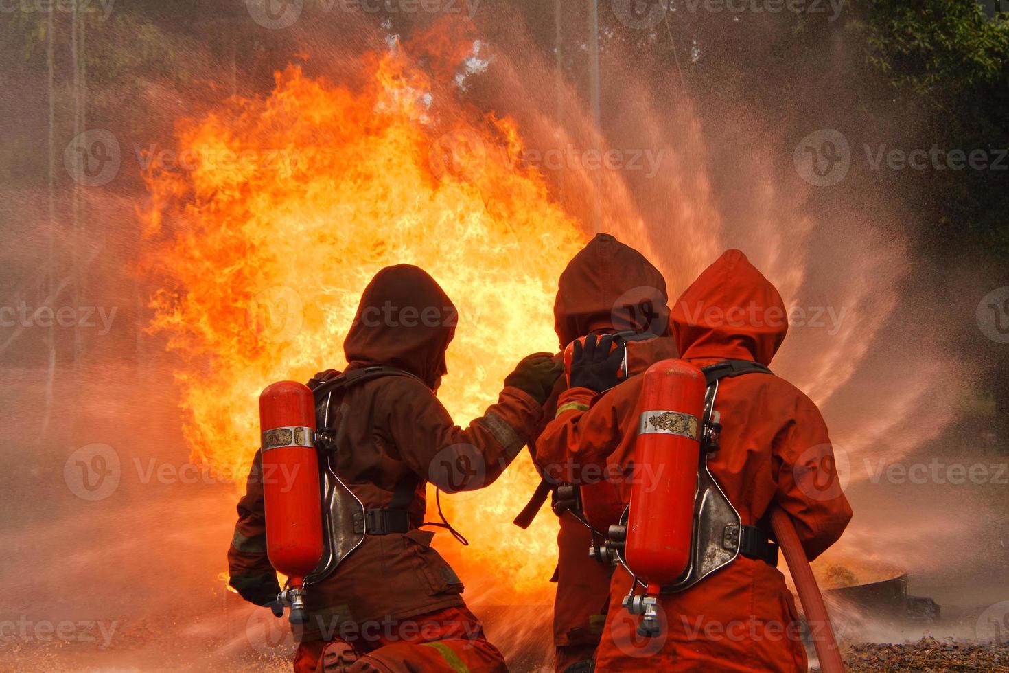 drei Feuerwehrleute, die mit einem Wasserwerfer ein Feuer löschen foto