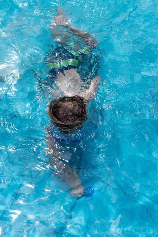 kleiner Junge, der unter Wasser mit Schutzbrillen im Pool schwimmt foto