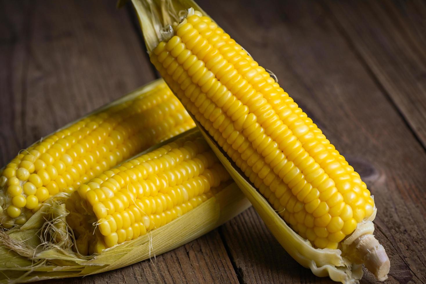 Zuckermais gekocht auf Holzhintergrund, reife Maiskolben gedünstet oder gekochter Zuckermais für veganes Abendessen oder Snack foto