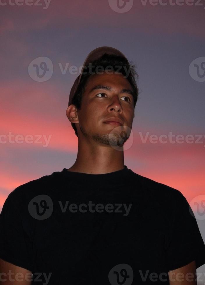 junger Mann mit gebräunter Haut, der in den Sonnenuntergang blickt foto