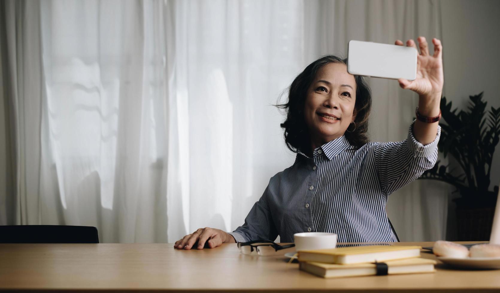 asiatische ältere ältere frauen lächeln und videoanruf im wohnzimmer zu hause. starke ältere ältere großmutter, die sich mit dem handy glücklich fühlt, kommunizieren mit der familie und genießen das leben im ruhestand im haus. foto