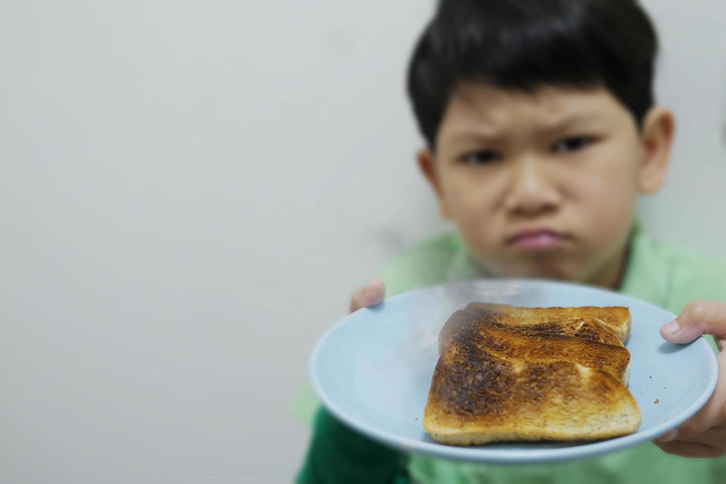 asiatische jungenshow über geröstetem verbranntem gegrilltem brotteller mit schlechtem unglücklichem stimmungsgesicht - essen frühstück enttäuschen konzept foto