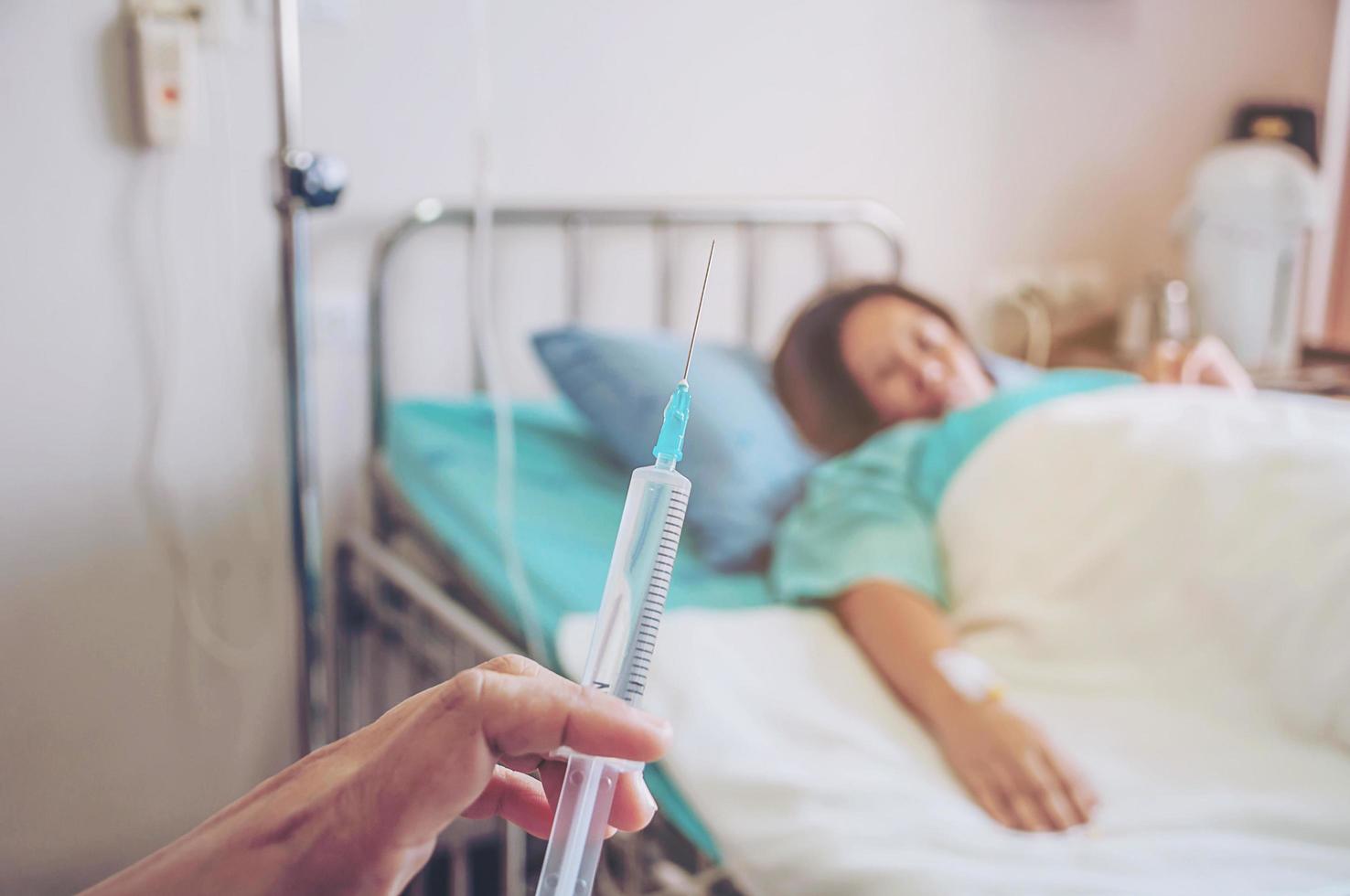 Arzt, der die Spritze in der Hand hält, bereit für die Injektion mit einem Patientenhintergrund im Krankenhaus foto