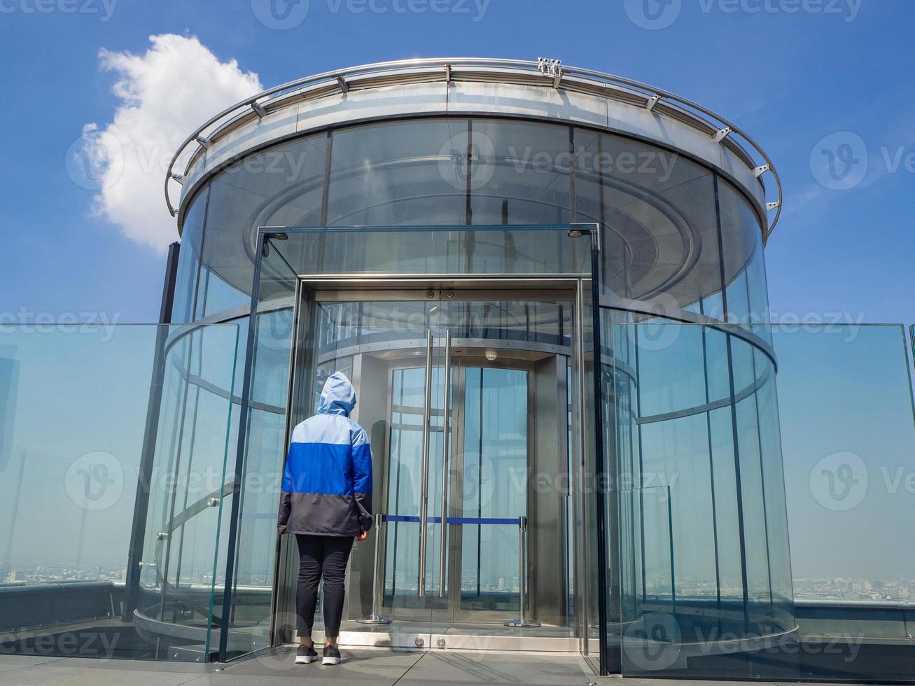 Rückansicht einer Frau, die mit dem Glas des Tunnels mit Aufzug steht foto