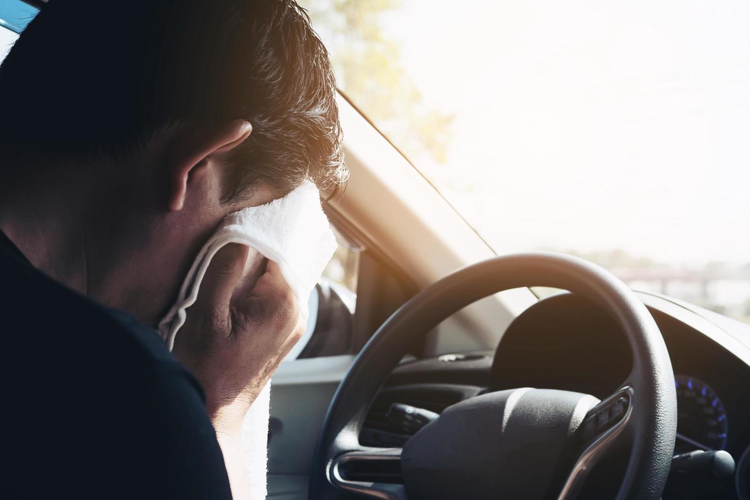 müder Mann, der sein Gesicht mit einem weißen kalten Erfrischungstuch abwischt, während er ein Auto fährt - lange Fahrt mit müdem Konzept foto