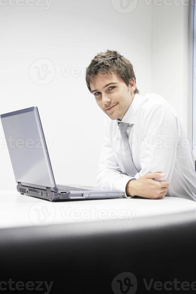 lächelnder Geschäftsmann, der mit Laptop am Schreibtisch sitzt foto