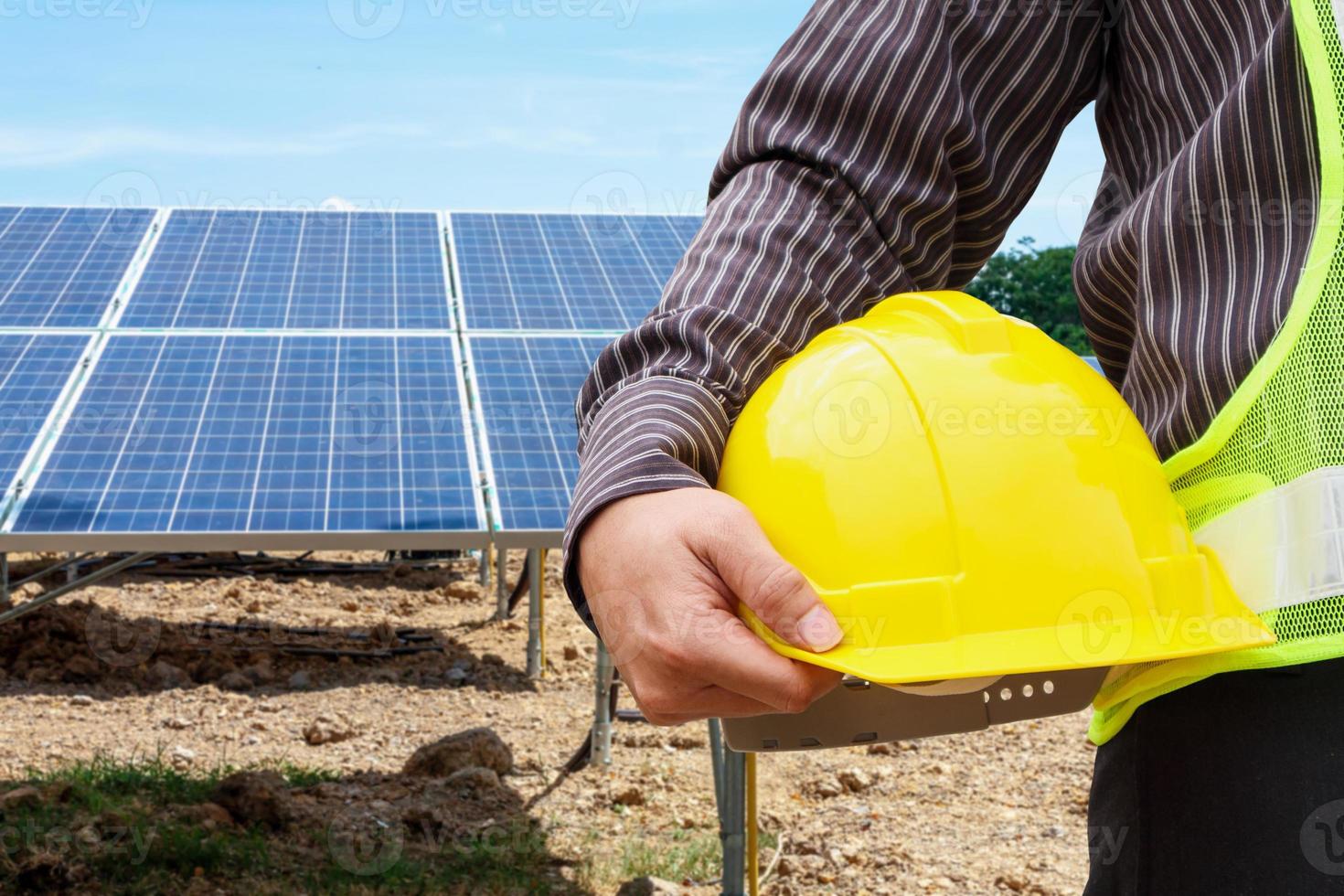 Junger Geschäftsmann-Ingenieur hält gelben Helm am Baustellenhintergrund des Solarpanel-Kraftwerks foto