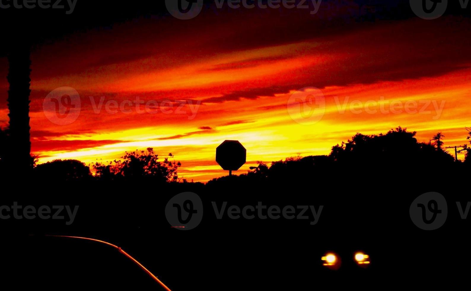 Sonnenuntergang mit Stoppschild gegen feuerroten Himmel umrissen foto