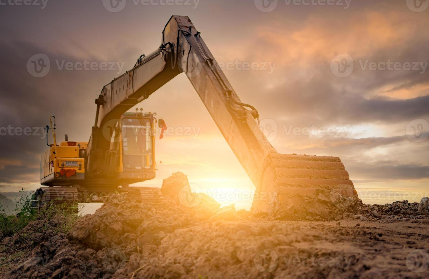 Bagger geparkt auf der Baustelle nach dem Graben von Erde. Planierraupe auf Sonnenunterganghimmel und Wolkenhintergrund. Bagger nach der Arbeit. Erdbewegungsmaschine auf der Baustelle in der Abenddämmerung. Bagger mit Schmutzeimer. foto