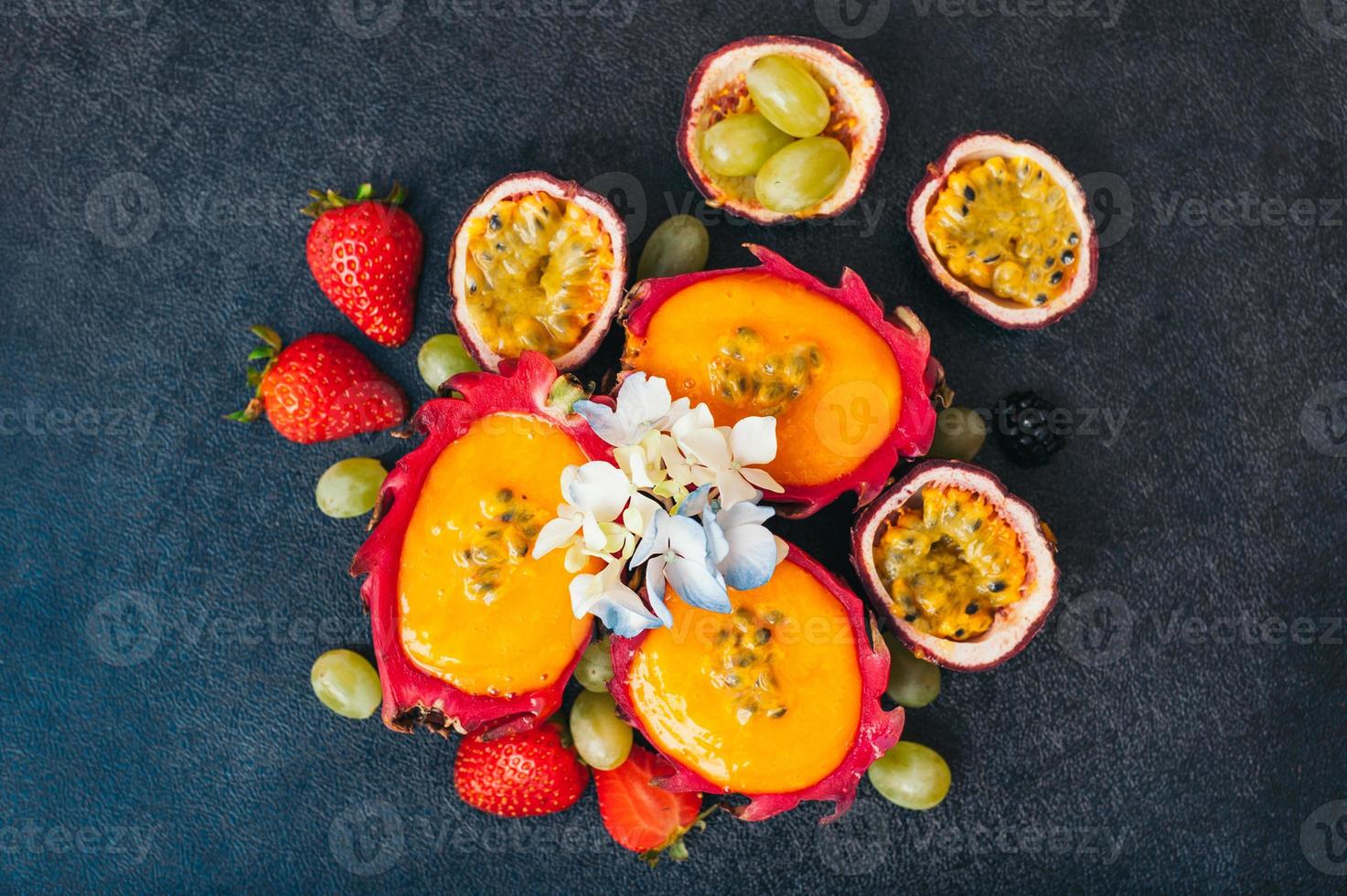 scheiben von drachenfrucht, roter reifer erdbeere und trauben auf dunklem hintergrund. Satz frisches Obst für die Zubereitung von vegetarischem Salat. ernährungs- und vitaminkonzept foto