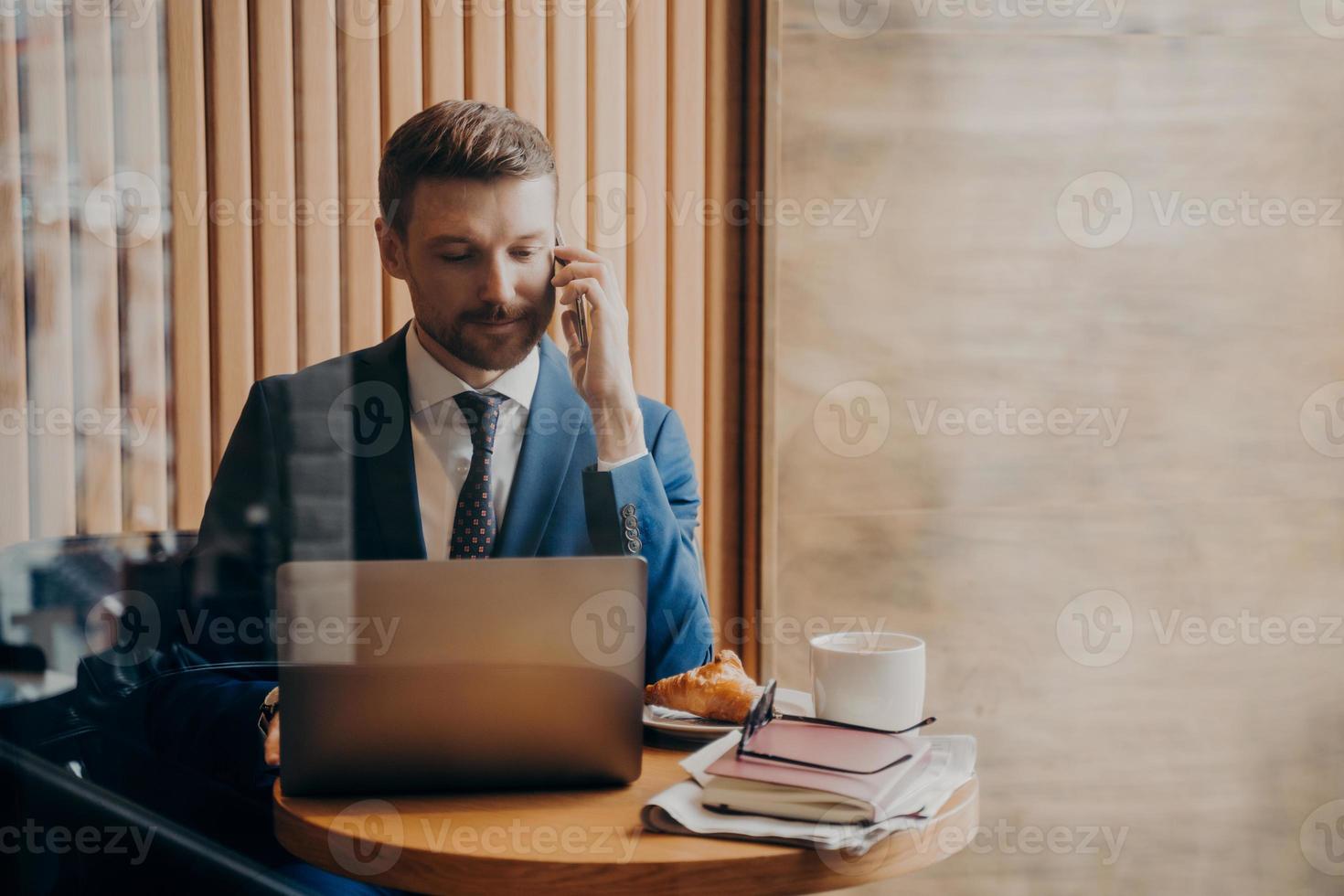 Porträt eines eleganten Finanzmanns im stilvollen Anzug, der im Café mit offenem Laptop sitzt foto