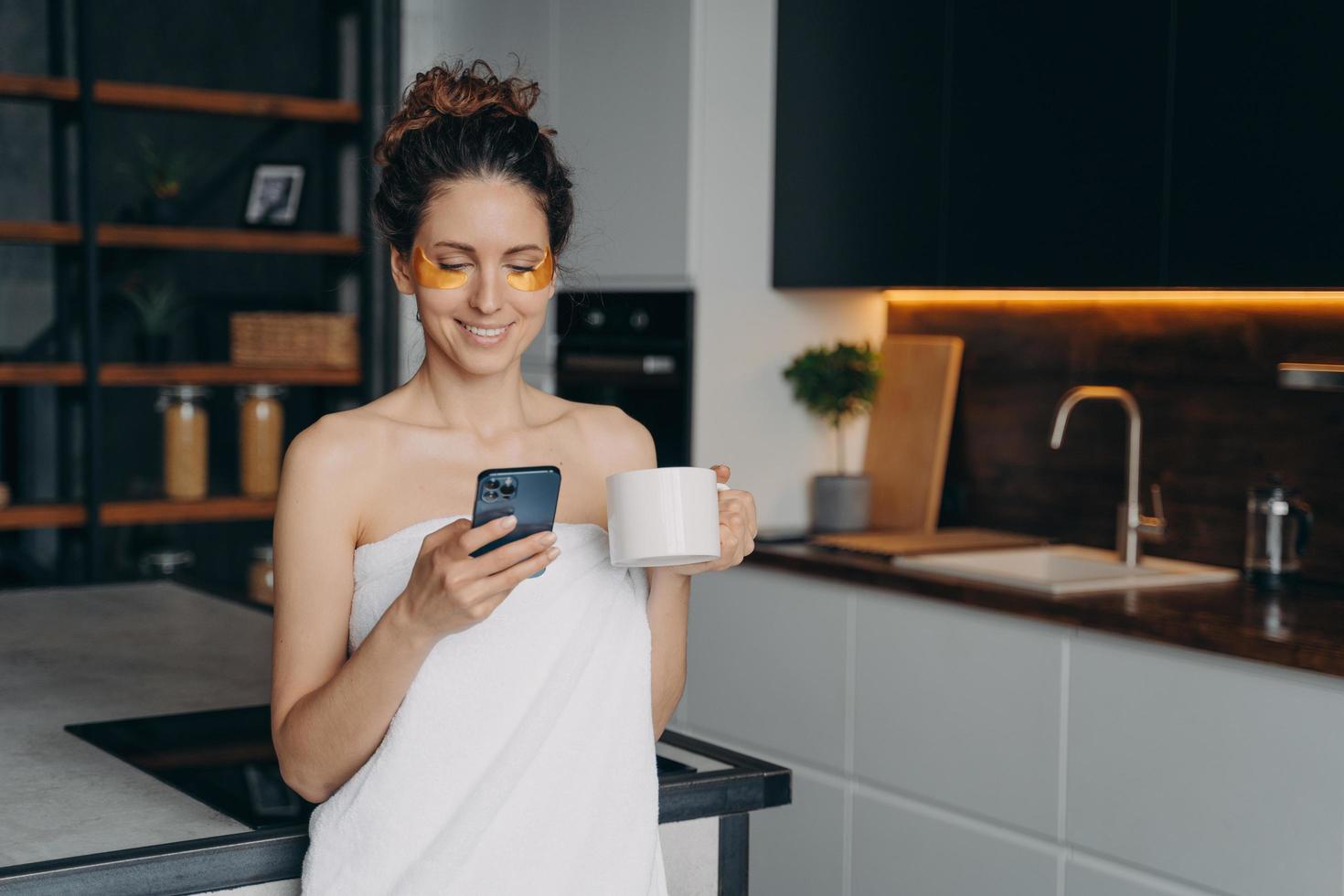 junge Frau trägt Anti-Falten-Augenklappen auf und entspannt sich zu Hause beim SMS-Schreiben am Telefon. foto