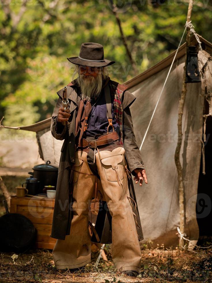 ein älterer Cowboy, der mit einer Waffe steht, um die Sicherheit des Lagers im westlichen Bereich zu bewachen foto