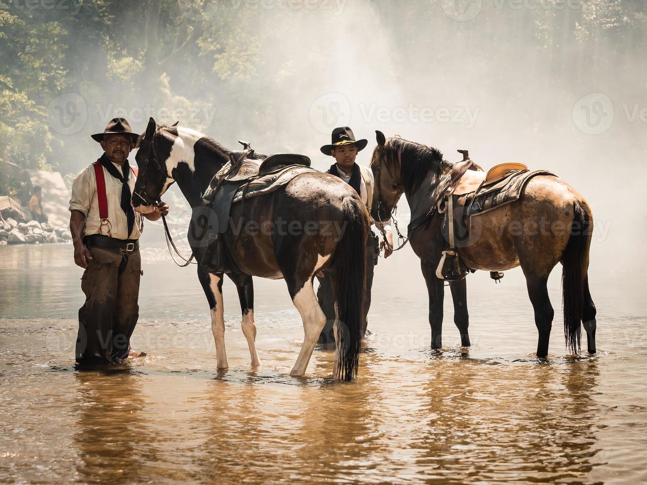 alter Cowboy und junge Kavallerie ruhen sich mit ihren Pferden im Bach aus, nachdem sie mit dem Baden fertig sind foto