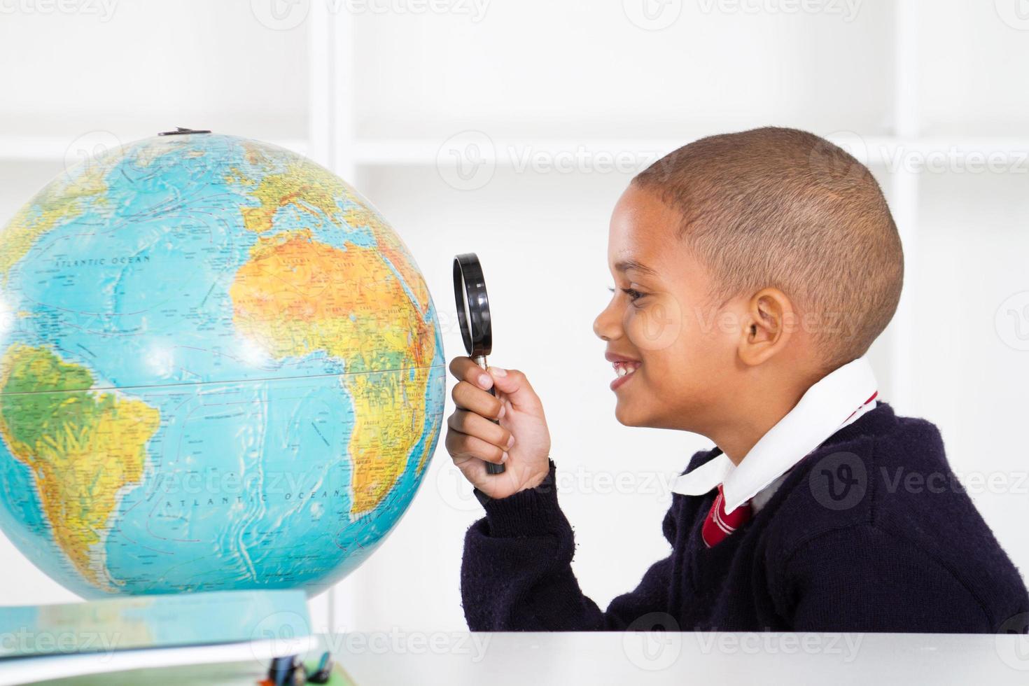 Schuljunge mit Lupe, die Globus betrachtet foto